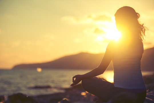 woman meditating in lotus pose on the beach at sunset