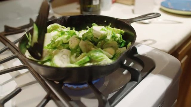 Close up on pan of sliced sprouts, cooking on a gas stove.  Hand held camera with bright lighting.  Slow motion recorded at 60fps.