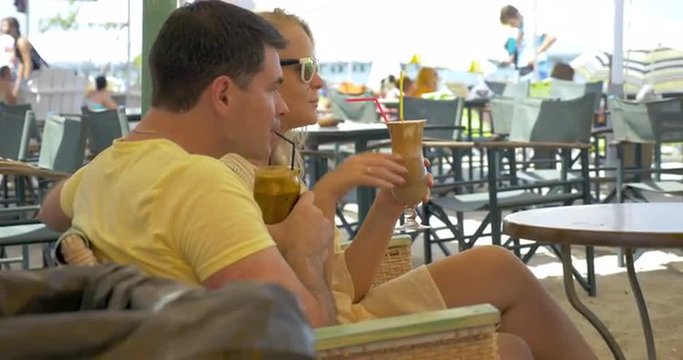 Young couple is having a date, they are sitting in outdoor cafe in sunny day and drinking ice coffee.