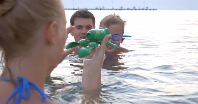 United family is playing with a swimming toy frog in the sea.