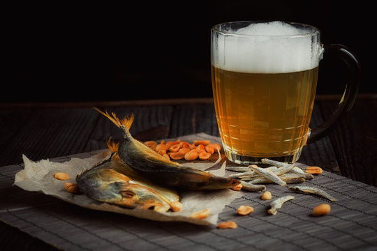 Beer and dried fish on dark wooden table.