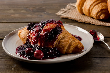 Sweet croissant with cherry jam on rustic background