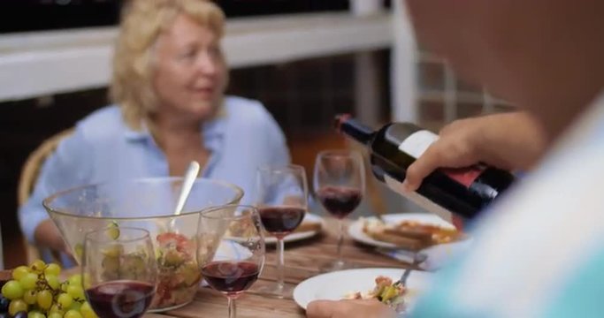 Late family dinner on the balcony. Focus on the man pouring red wine and then all of them clanging glasses