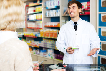Fototapeta na wymiar Helpful pharmacist serving young woman in pharmacy