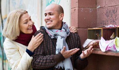 Portrait of loving mature couple feeding birds in cage