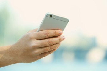 A female hand holding a mobile phone outdoors, on blurred background
