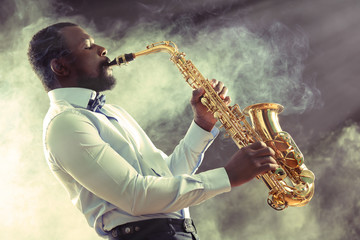 African American jazz musician playing the saxophone against smoky background