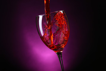 Wine pouring in glass on dark purple background