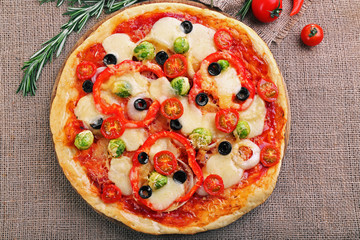 Delicious pizza with cheese and vegetables on sackcloth background