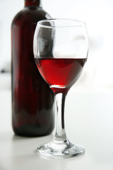 Glass of red wine with bottle on blurred interior background