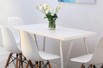 Modern dining room. White chairs and table with bouquet of flowers, abstract picture on the wall