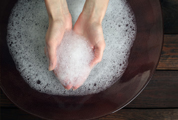 Woman washing hands in bowl on wooden background