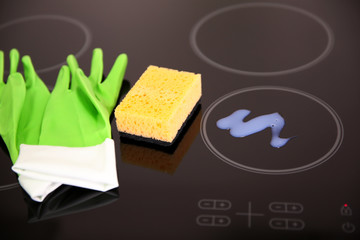 Detergent with protective gloves and sponge on electric hob closeup