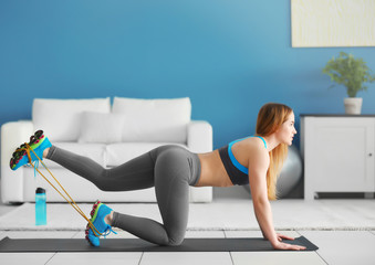 Young sportswoman doing exercises with rubber band and dumbbells on a mat at home