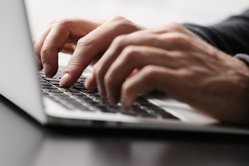 Male hands typing on laptop keyboard at table closeup