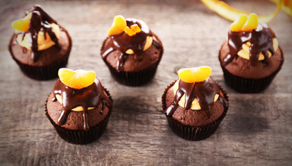 Tasty cupcakes with slice of mandarin and chocolate on wooden background