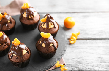 Tasty cupcakes with slice of mandarin and chocolate on slate plate over light wooden background