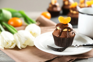 Tasty cupcake with slice of mandarin and chocolate on a plate over light wooden background