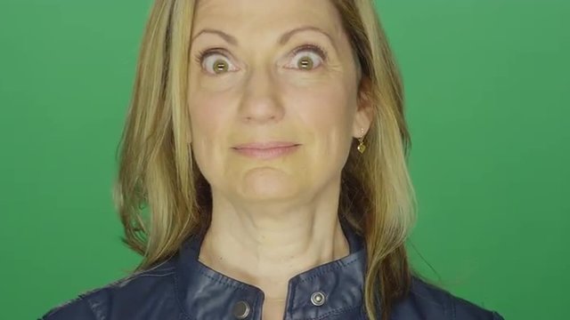 Beautiful middle aged woman making funny faces, on a green screen studio background