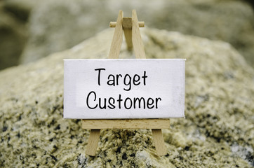 conceptual image,  word TARGET CUSTOMER on white canvas frame and wooden tripod stand. blur rock textures background