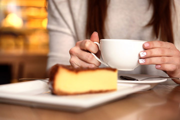 Tasty cheesecake on table in cafe or restaurant and woman with cup of tea