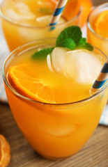 Delicious tangerine cocktails with ice, mint and straws served on a wooden table, close up