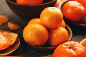 Peeled and unpeeled tangerines in wooden spoons and bowls, close up