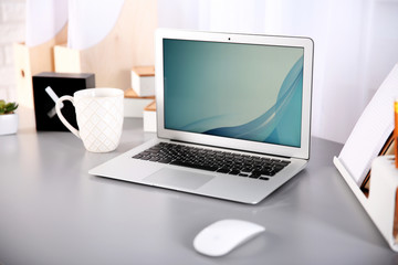 Workplace with laptop, table, mouse and cup beside the window