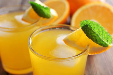 Two orange juices with ice and orange on, closeup