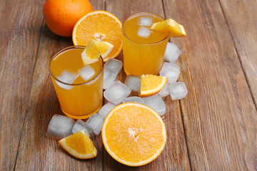 Two orange juices with cubes of ice and orange on wooden table background