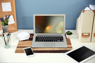 Fototapeta premium Workplace with different devices, stationery and table on blue wall background