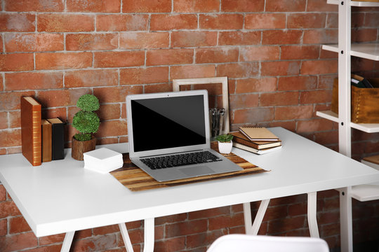 Workplace with laptop, table and bookcase on brick wall background