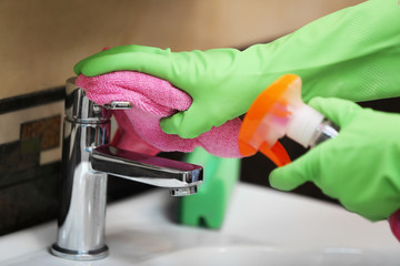 Female hands with rag and detergent spray cleaning a tap in the bathroom