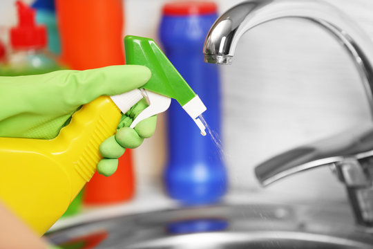 Female hand with detergent spray cleaning a sink in the kitchen