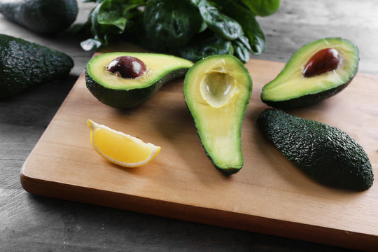 Sliced avocado with lemon and spinach on wooden cutting board