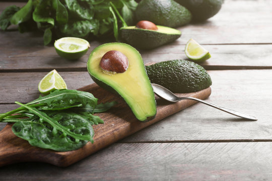 Sliced avocado with lime, spinach and arugula on wooden cutting board