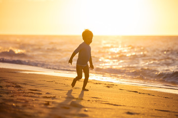 Happy little boy running on beach. Sunset light.