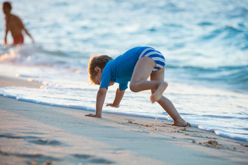 Little boy having fun on the beach. Crawling and playing along water's edge. Motion blur.