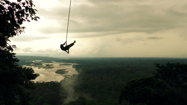 A high-angle shot of a meandering river cutting through a vast lush jungle in the Ecuadorian Amazon under a cloudy sky, mist rising from the forest as sunlight breaks through the clouds.