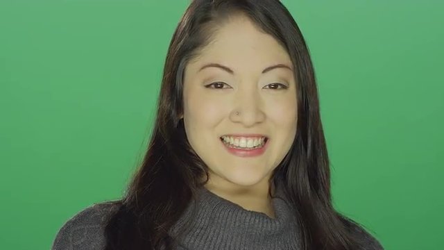 Beautiful young Asian woman smiling and flirting, on a green screen studio background
