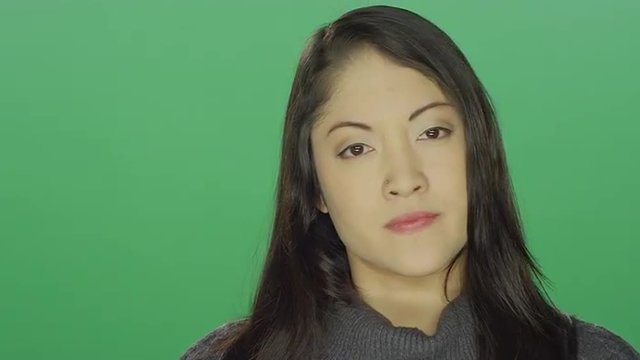 Beautiful young Asian woman looking annoyed and angry, on a green screen studio background