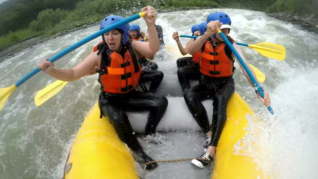 A group of adventurers in a yellow raft navigate turbulent white-water rapids on the Pastaza River near Banos, Ecuador, paddling vigorously in a low immersive onboard shot of teamwork.