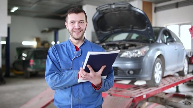 View of a Young attractive mechanic working at the garage. Handsome smiling mechanic.