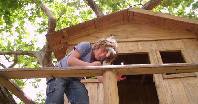 Boy repairing his wooden treehouse with a hammer and nail