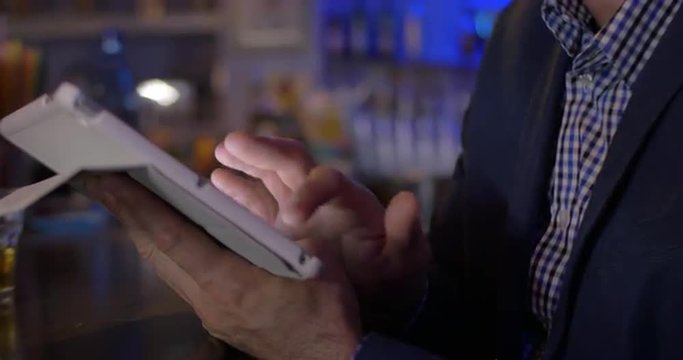 Businessman using tablet computer sitting at the bar counter. Doing the job and relaxing with drink