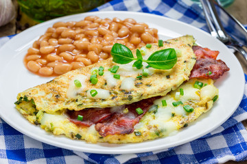 Bacon stuffed omelette with backed beans on a white plate
