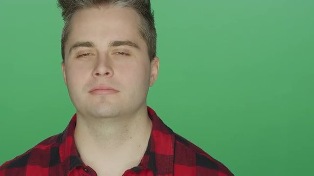 Young man staring and looking confused, on a green screen studio background
