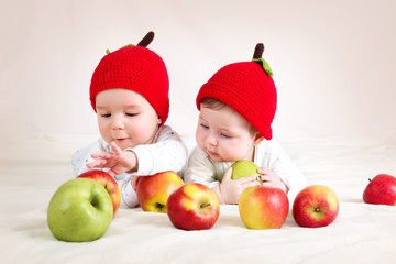 Fototapeta na wymiar two cute babies lying in hats on soft blanket with apples