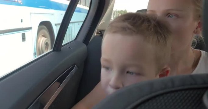 Little boy and mother travelling in car. Boy drinking from bottle, kissing mother and looking through the window