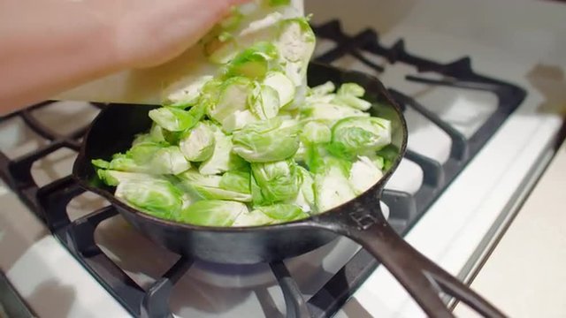 Close up on cook's hands pushing sprouts into a pan on top of gas stove, ready to fry them.  Hand held camera, slow motion recorded at 60fps.